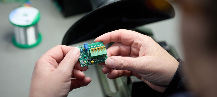 Manuelle Prüfung einer elektronischen Baugruppe bei GLÜCK Industrie-Elektronik im Rahmen der E²MS Qualitätssicherung.