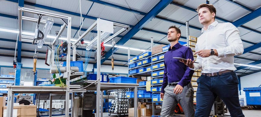 Zwei Mitarbeiter von Glück Elektronik gehen durch die Produktionshalle und begutachten eine Montageanlage.